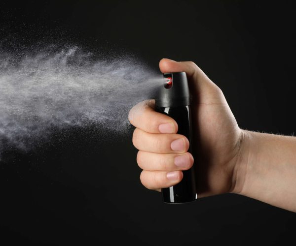 Man using pepper spray on black background, closeup